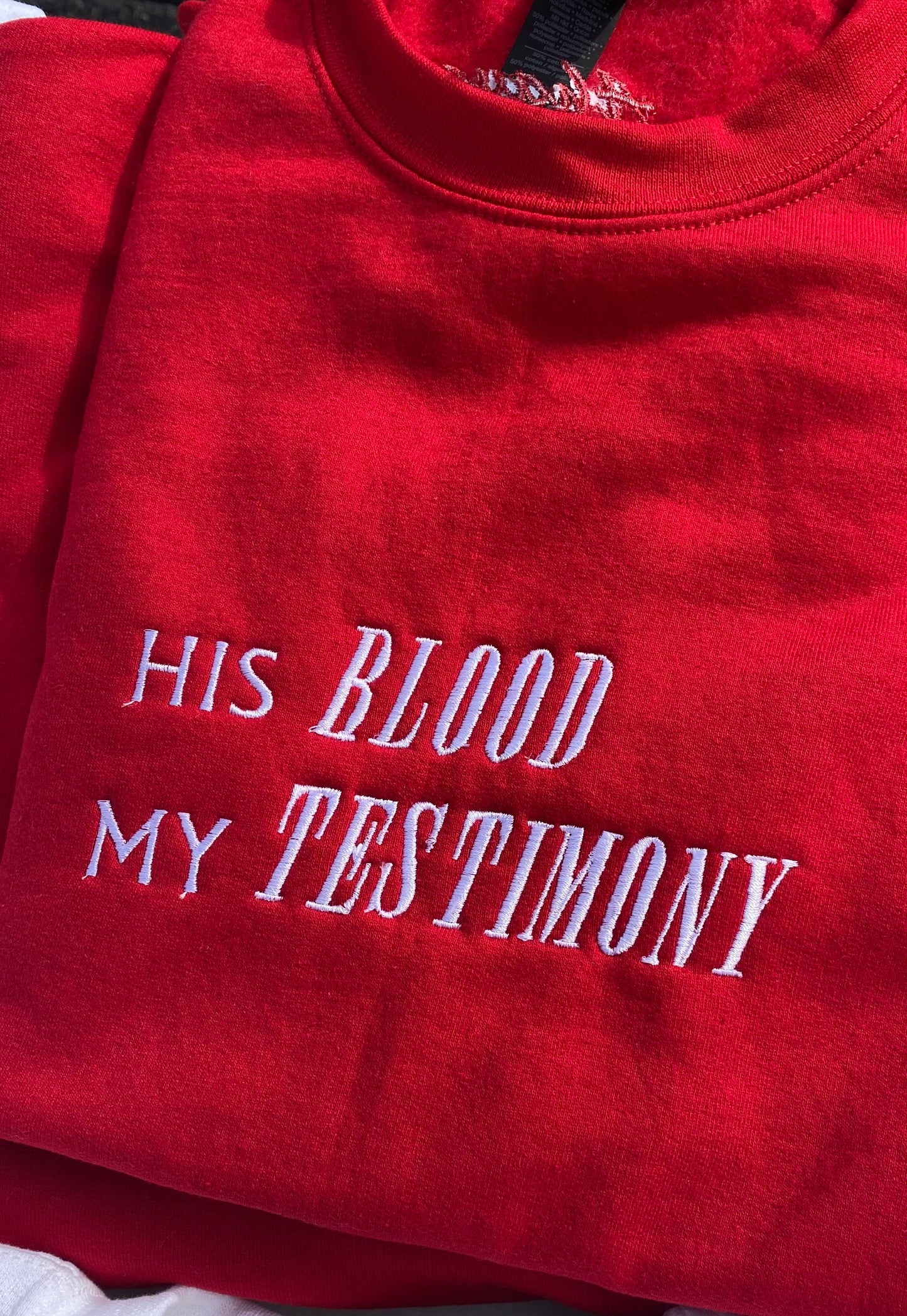 Red sweatshirt with the text 'HIS BLOOD MY TESTIMONY' embroidered in white.