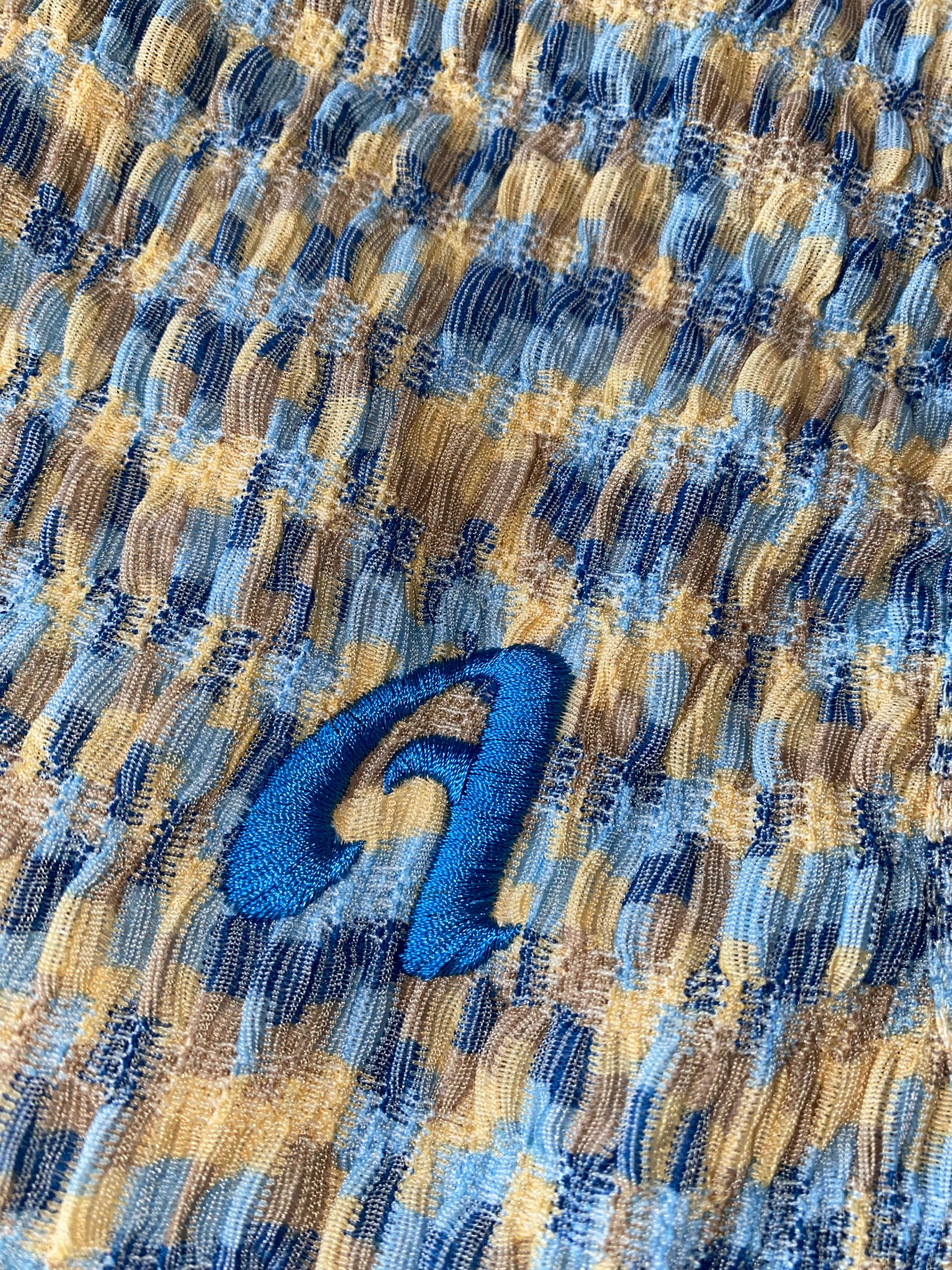 A close-up image of a blue and multicolored tank top with a bright blue letter 'A' on the left chest.