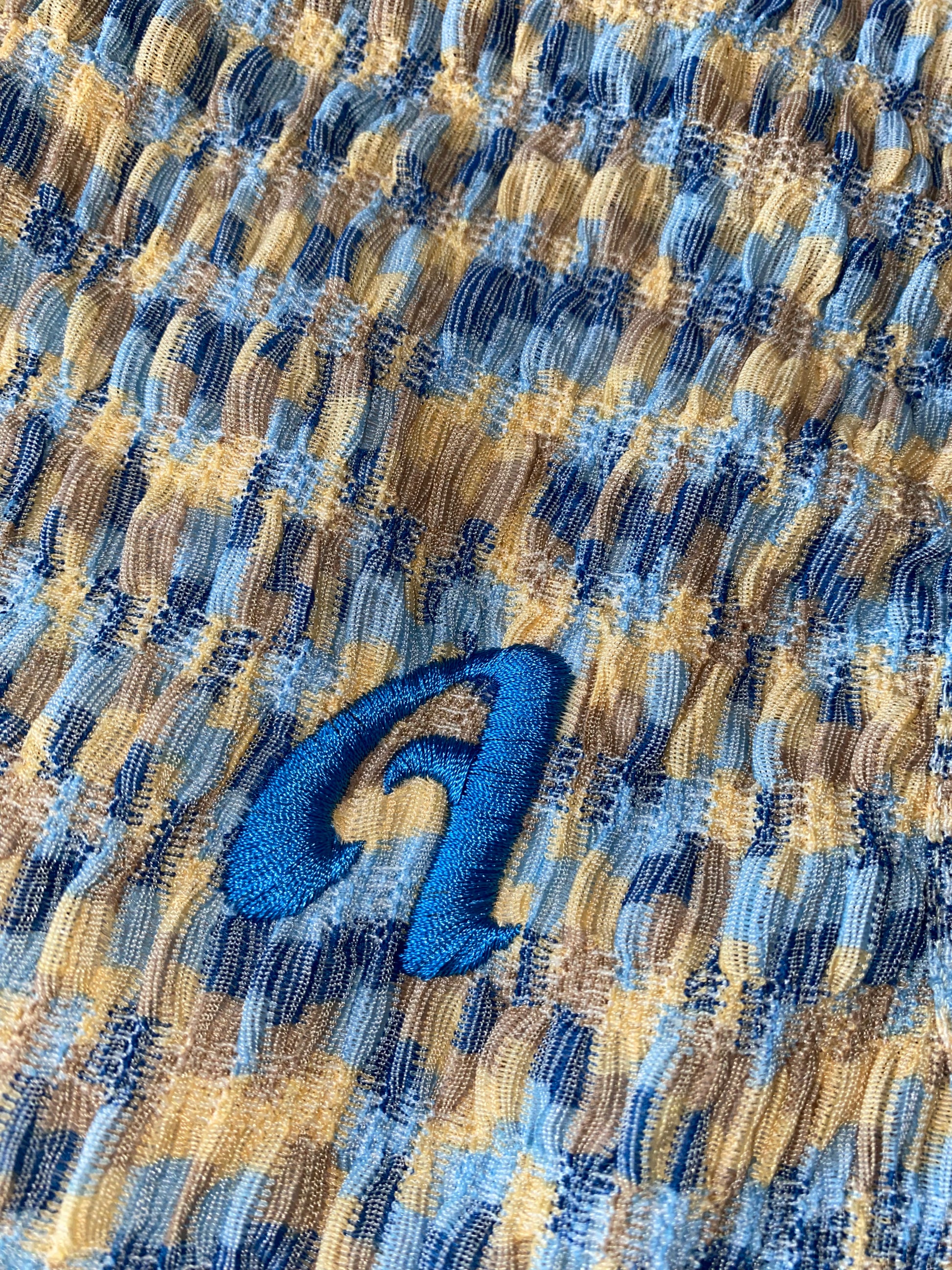 A close-up image of a blue and multicolored tank top with a bright blue letter 'A' on the left chest.