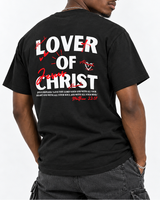 A man wearing a black graphic t-shirt from the back, featuring the text 'LOVER OF JESUS CHRIST' in white and red with a Bible verse printed below. He is also wearing black sunglasses and dark gray cargo pants against a plain white background.