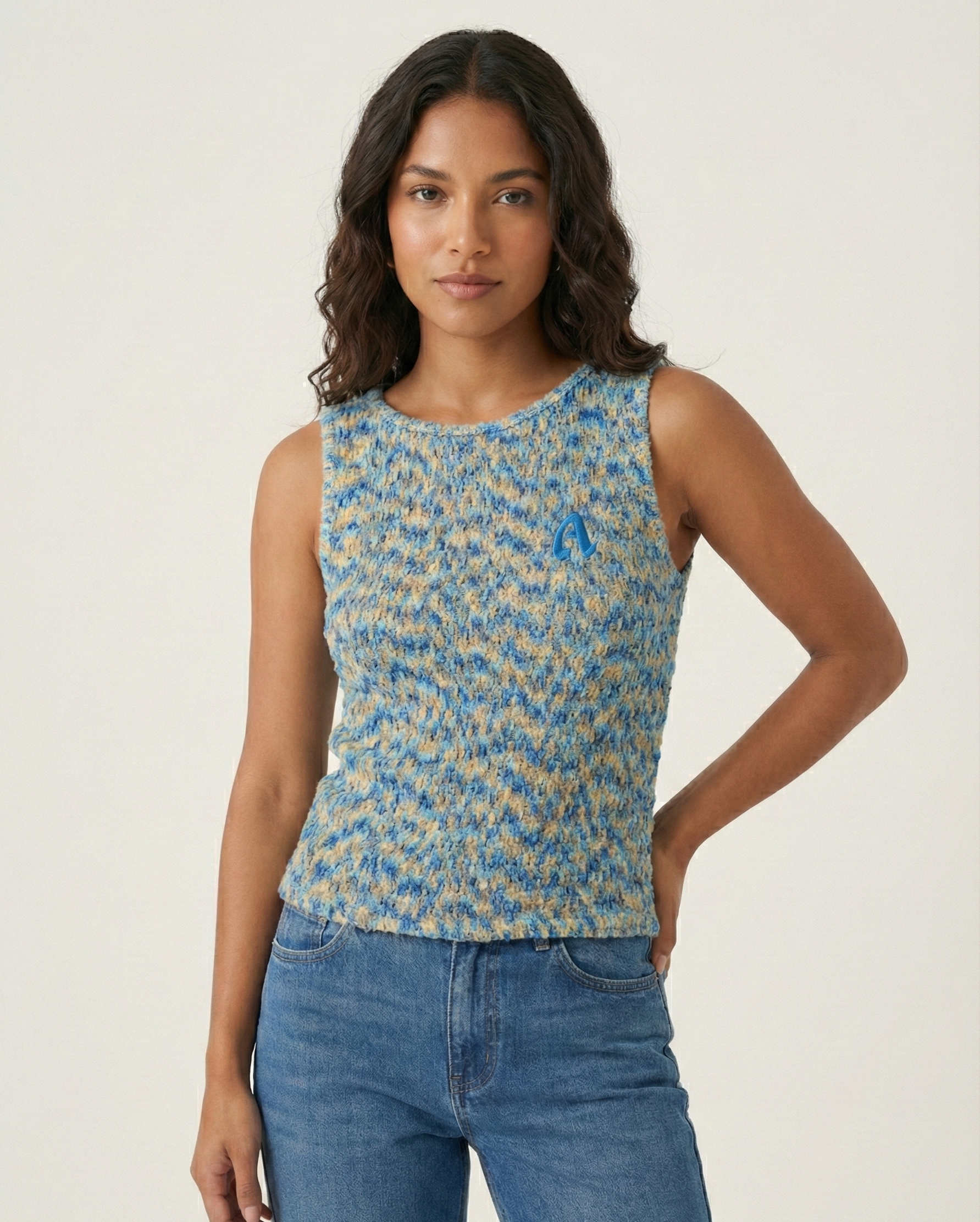 Woman wearing a blue patterned sleeveless top and jeans on a plain background