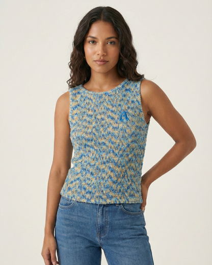 Woman wearing a blue patterned sleeveless top and jeans on a plain background