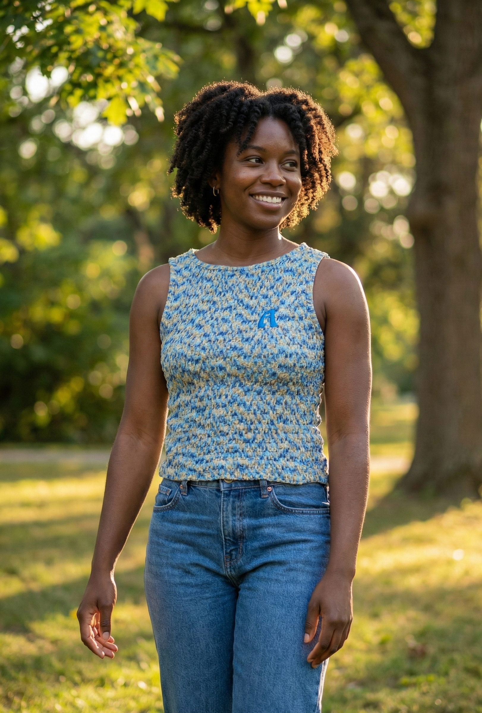 Woman wearing a blue floral top and jeans standing in a park with trees and sunlight.