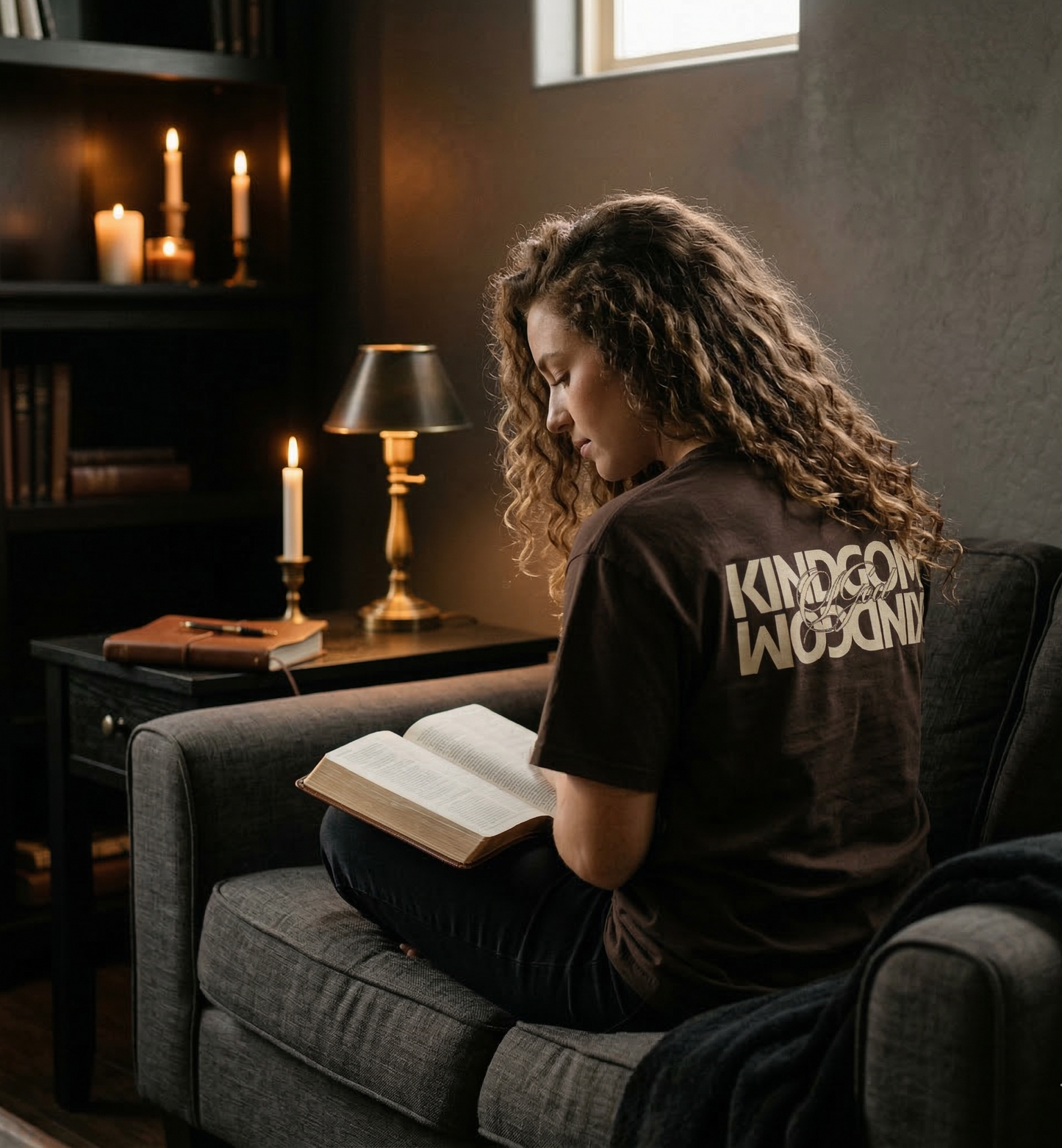 Woman sitting on a couch reading a book in a dimly lit room with candles and books.