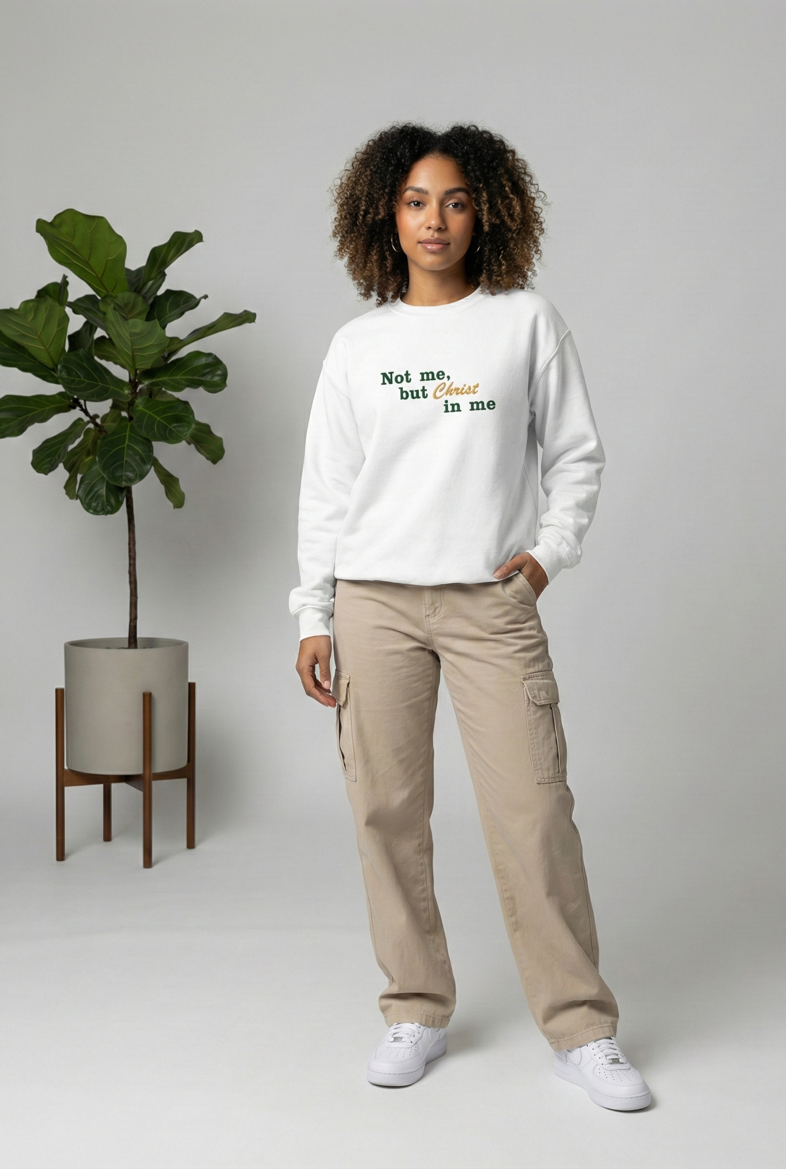 Person wearing a white sweatshirt with text, standing in a minimalistic room with a plant.